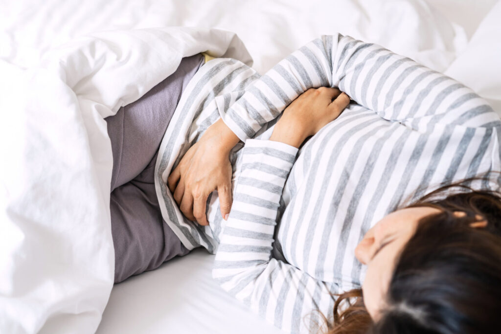 Young woman having stomach ache on the bed. Periods cramp problems concept