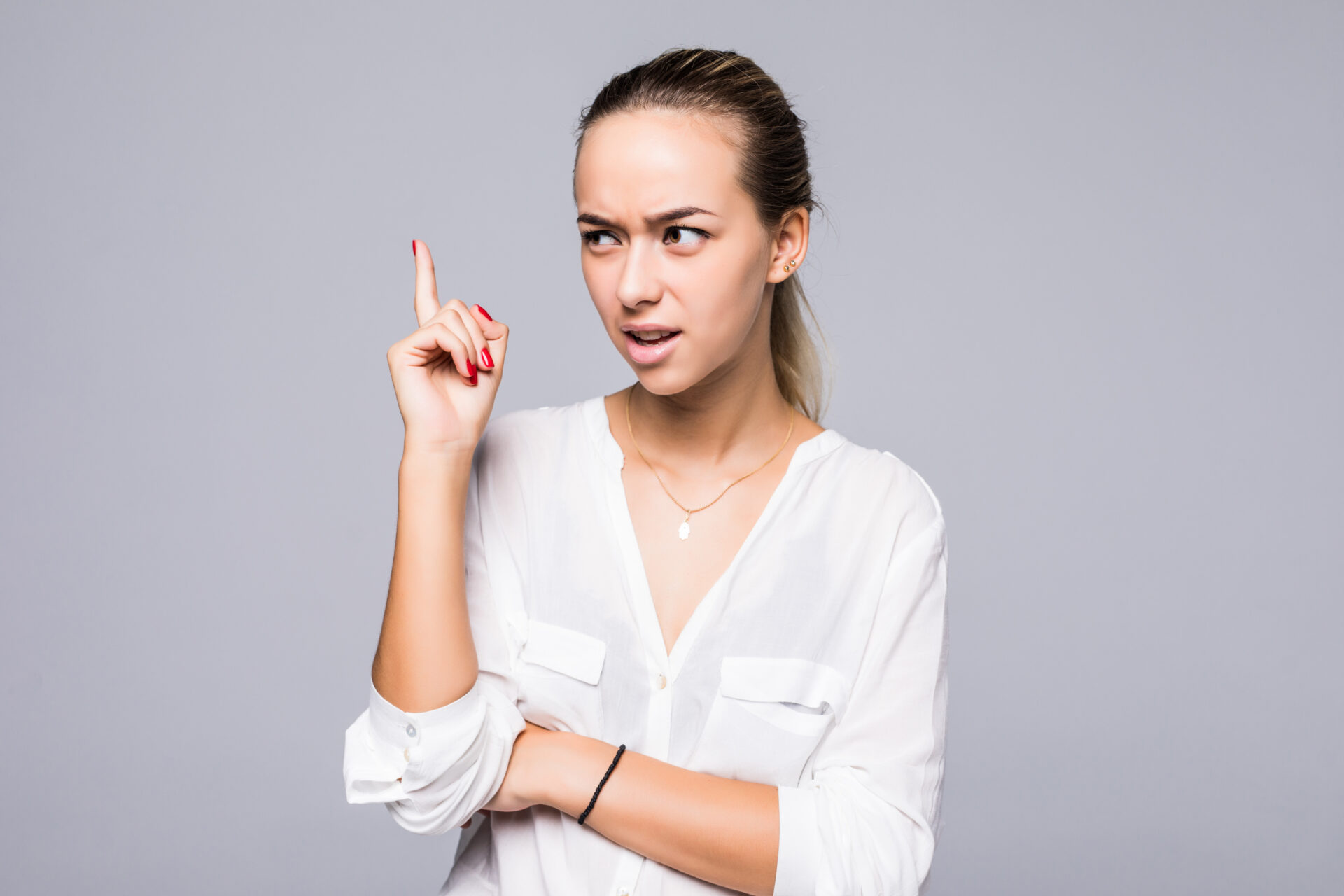 Portrait serious, frowning, angry, grumpy young woman pointing finger upwards, scolding someone isolated grey background Portrait serious, frowning, angry, grumpy young woman pointing finger upwards, scolding someone isolated grey background