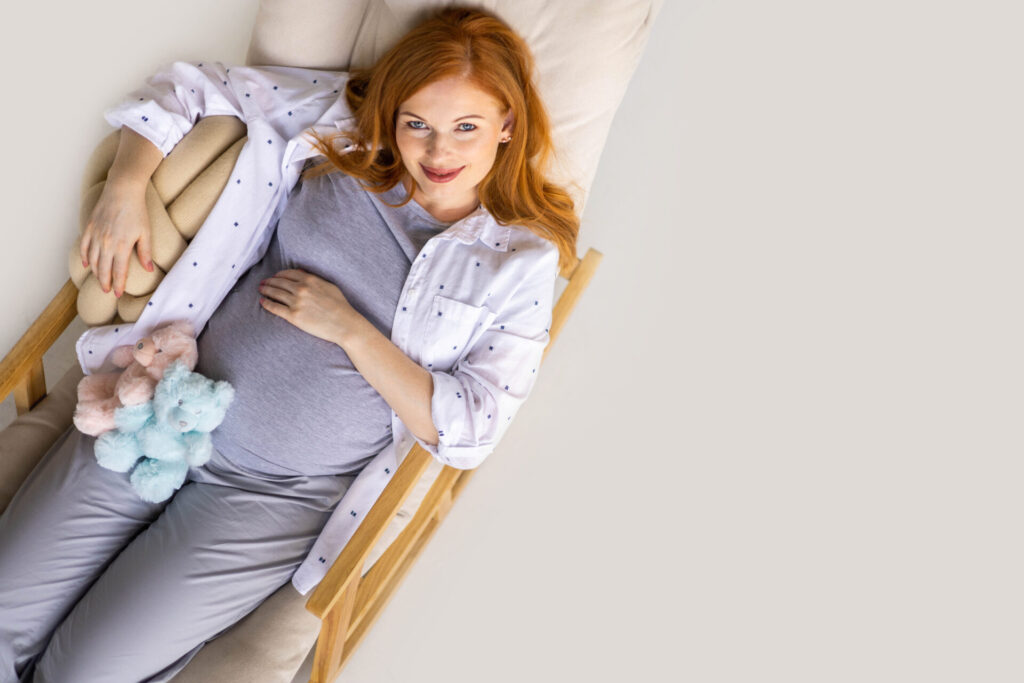 Top view happy young redhead pregnant woman lying on comfortable armchair